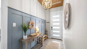 A hallway with a wooden bench, a potted plant, a wall-mounted wreath, and a chandelier.