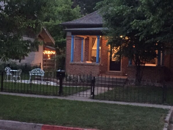 Une petite maison en briques avec un porche, une cour clôturée et un banc.