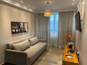 A modern living room with a sofa, a wooden side table with a plant, a TV mounted on the wall, and artwork on the wall.