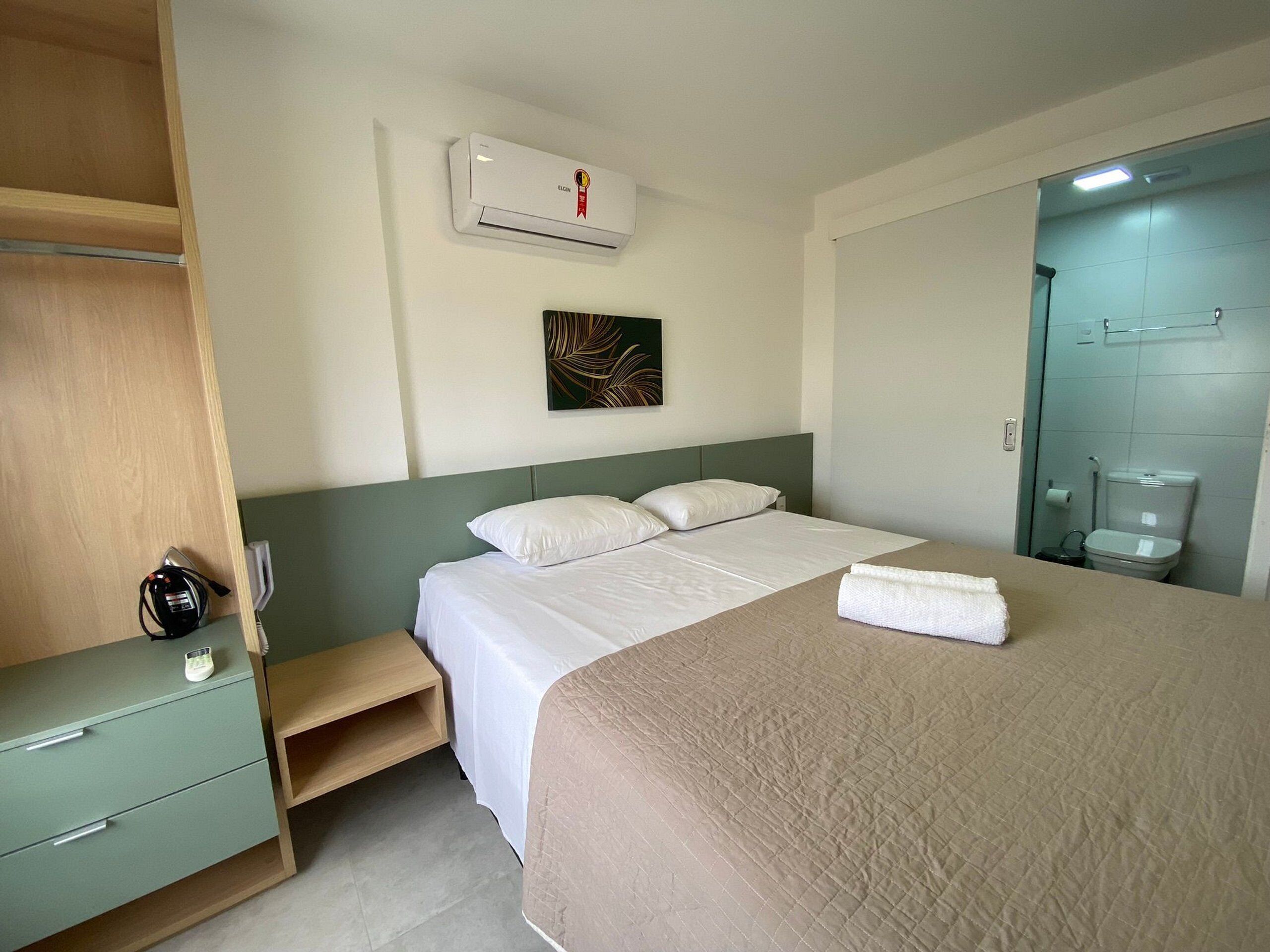 Ein Hotelzimmer mit Bett, Nachttisch, Kleiderschrank, Badezimmer mit Toilette und Waschbecken sowie einer Klimaanlage.