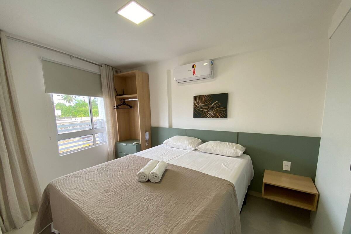 Une chambre d’hôtel comprenant un lit, une table de chevet, une commode, une armoire, une fenêtre avec des rideaux et un climatiseur fixé au mur.
