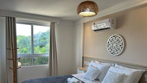 Una habitación de hotel con una cama, un ventanal con cortinas, un equipo de aire acondicionado y un adorno en la pared.