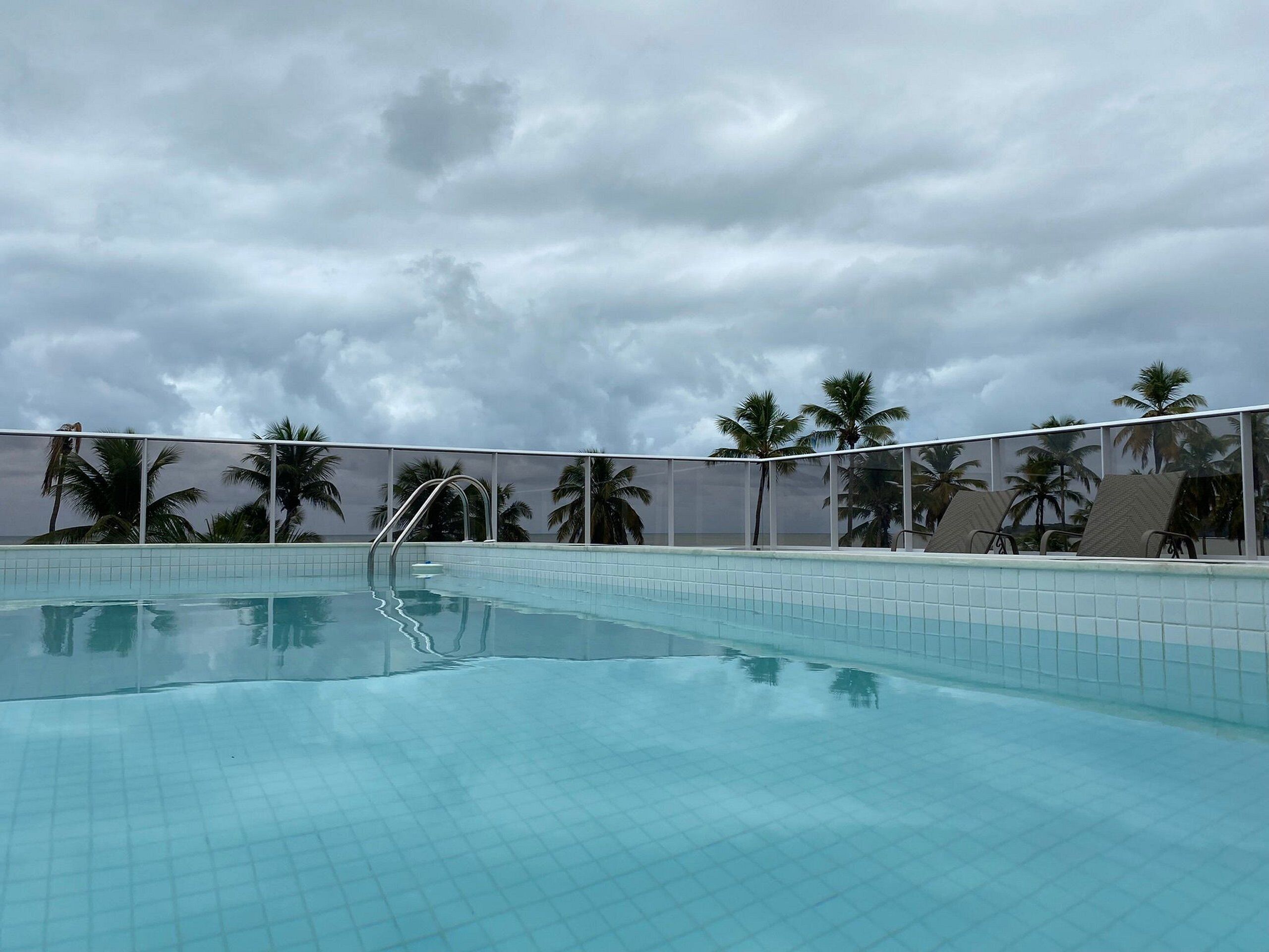 Una piscina con piso de baldosas y una escalera de metal.