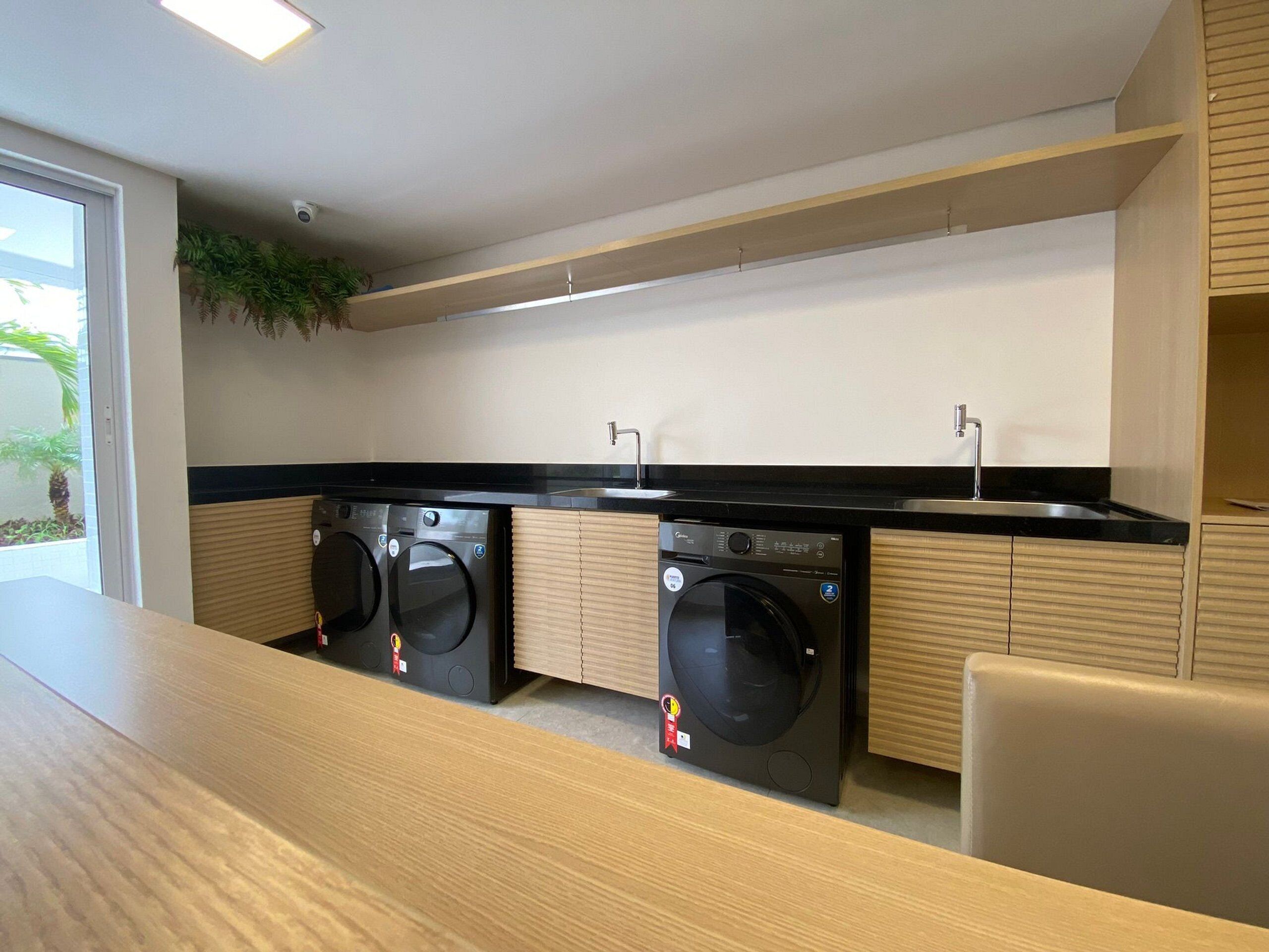 A modern laundry room with two front-loading washing machines, a sink, and a wooden counter.