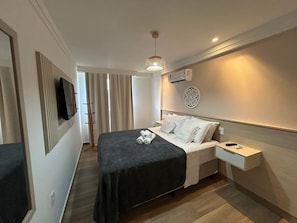 Hotellihuone, jossa on sänky, yöpöydät, televisio, koristeellinen seinäelementti ja kattovalaisin.