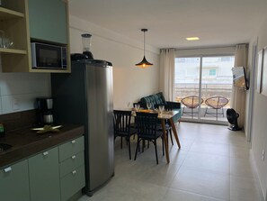 Moderni keittiö, jossa on jääkaappi, mikroaaltouuni ja kahvinkeitin. Keittiössä on ruokailutila, jossa on pöytä ja tuolit, sekä parveke, jossa on myös tuoleja.