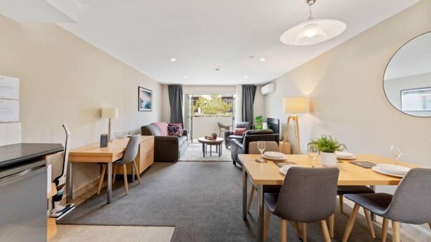 Moderni hotellihuone, jossa on ruokailutila, sohva, pieni pöytä ja suuri peili.