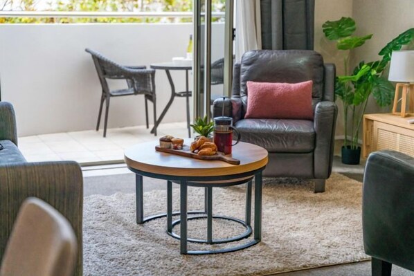 Uma sala de estar aconchegante com uma poltrona de couro, uma mesa de centro redonda com petiscos e vista para a varanda.