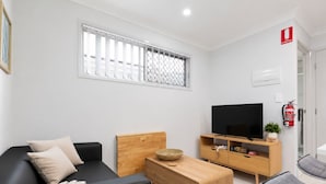 A modern living room with a black sofa, wooden coffee table, and a TV on a wooden stand. - Clean 1 Bdr Apt w/ AC | Covered Parking | 539F1 (Rocklea)