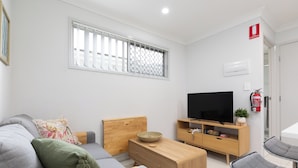 A modern living room with a grey sofa, wooden coffee table, and a flat-screen TV. - Clean 1 Bdr Apt w/ AC | Covered Parking | 539F1 (Rocklea)