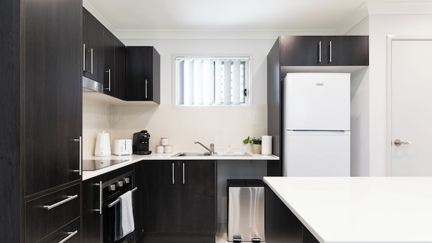 A modern kitchen with dark cabinetry, a stainless steel refrigerator, and a white countertop. - Clean 1 Bdr Apt w/ AC | Covered Parking | 539F1 (Rocklea)