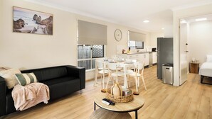 Una sala moderna con un sofá negro, una mesa de comedor con sillas, una zona de cocina y un ventanal con vistas a la playa.