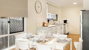 Una cocina moderna con armarios blancos, un refrigerador de acero inoxidable y un comedor con vajilla y sillas blancas.