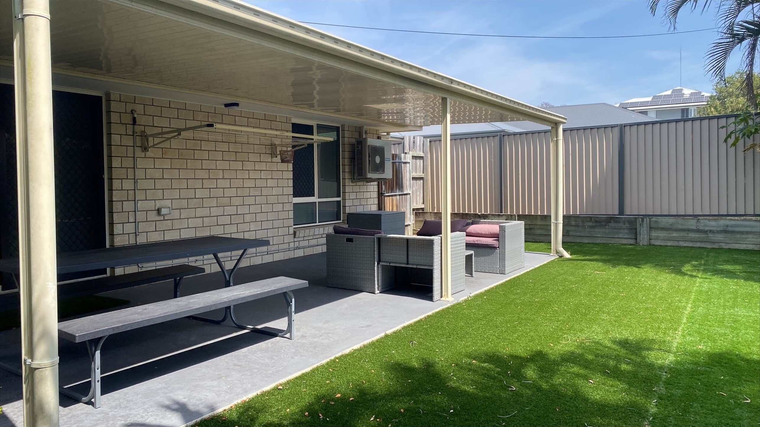 A covered outdoor patio with a brick wall, a table, benches, and wicker furniture.