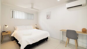 A bedroom with a bed, bedside tables, a desk, a chair, an air conditioner, a ceiling fan, and a window with blinds. - 1 Bdr Apt w/ AC | Kitchen | Parking | 131AF1 (Rocklea)
