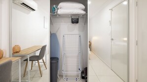 A compact room with a bed, a small table with chairs, a drying rack, and a trash bin. - 1 Bdr Apt w/ AC | Kitchen | Parking | 131AF1 (Rocklea)