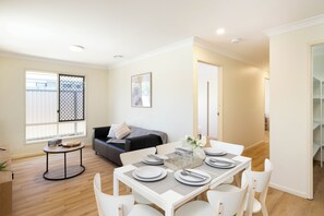 Un coin repas avec une table dressée pour quatre personnes, un canapé et une fenêtre avec des stores.