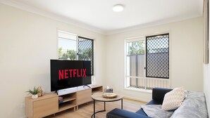 A modern living room with a flat-screen TV, a wooden cabinet, a round coffee table, and a blue sofa. - Clean Acacia Ridge 1BR | Kitchen | 12AS1 (Acacia Ridge)