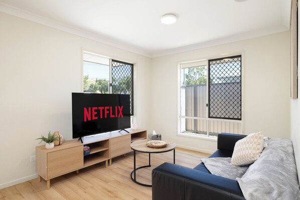 A modern living room with a flat-screen TV, a wooden cabinet, a round coffee table, and a blue sofa. - Acacia Ridge 3BR | Spacious & Easy Location | 12AS3 (Acacia Ridge)