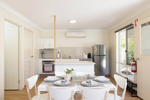 A modern kitchen with white cabinets, a stainless steel refrigerator, and a dining area with white chairs and a table set for four. - Acacia Ridge 3BR | Spacious & Easy Location | 12AS3 (Acacia Ridge)