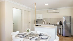 A modern kitchen with white cabinets, a stainless steel refrigerator, and a dining area with white chairs and a table set for four. - Acacia Ridge 3BR | Spacious & Easy Location | 12AS3 (Acacia Ridge)