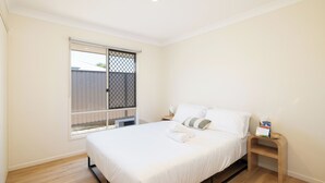 A bedroom with a bed, a nightstand, a window with a metal screen, and a view of a fence. - Acacia Ridge 3BR | Spacious & Easy Location | 12AS3 (Acacia Ridge)