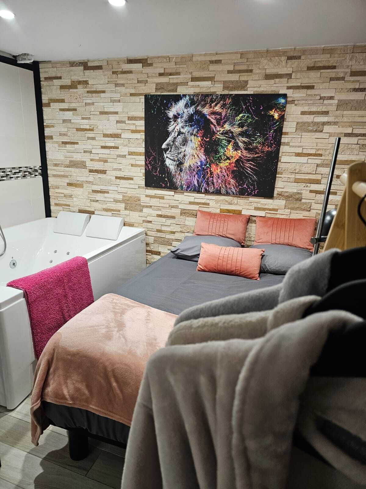 A modern bedroom with a stone-patterned wall, a large abstract painting, a bathtub, and a bed with multiple pillows.