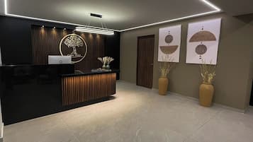 Una zona d'entrada moderna amb una taula de recepció negra, un logotip a la paret i dos vasos amb plantes seques.