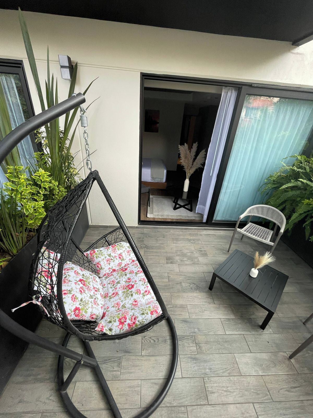A patio with a hanging chair, a small table, and a chair. There is a sliding glass door leading to an interior space.