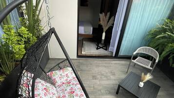 A patio with a hanging chair, a small table, and a chair. There is a sliding glass door leading to an interior space.