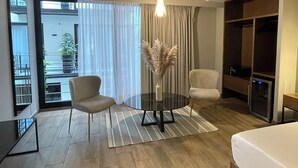 Una habitación de hotel moderna con una mesa de vidrio, dos sillas, un ventanal con cortinas, una lámpara colgante y un armario.