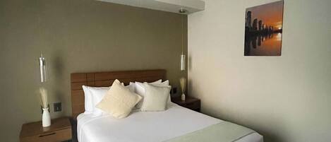 Een hotelkamer met een groot bed, een nachtkastje met een lamp en een schilderij aan de muur.