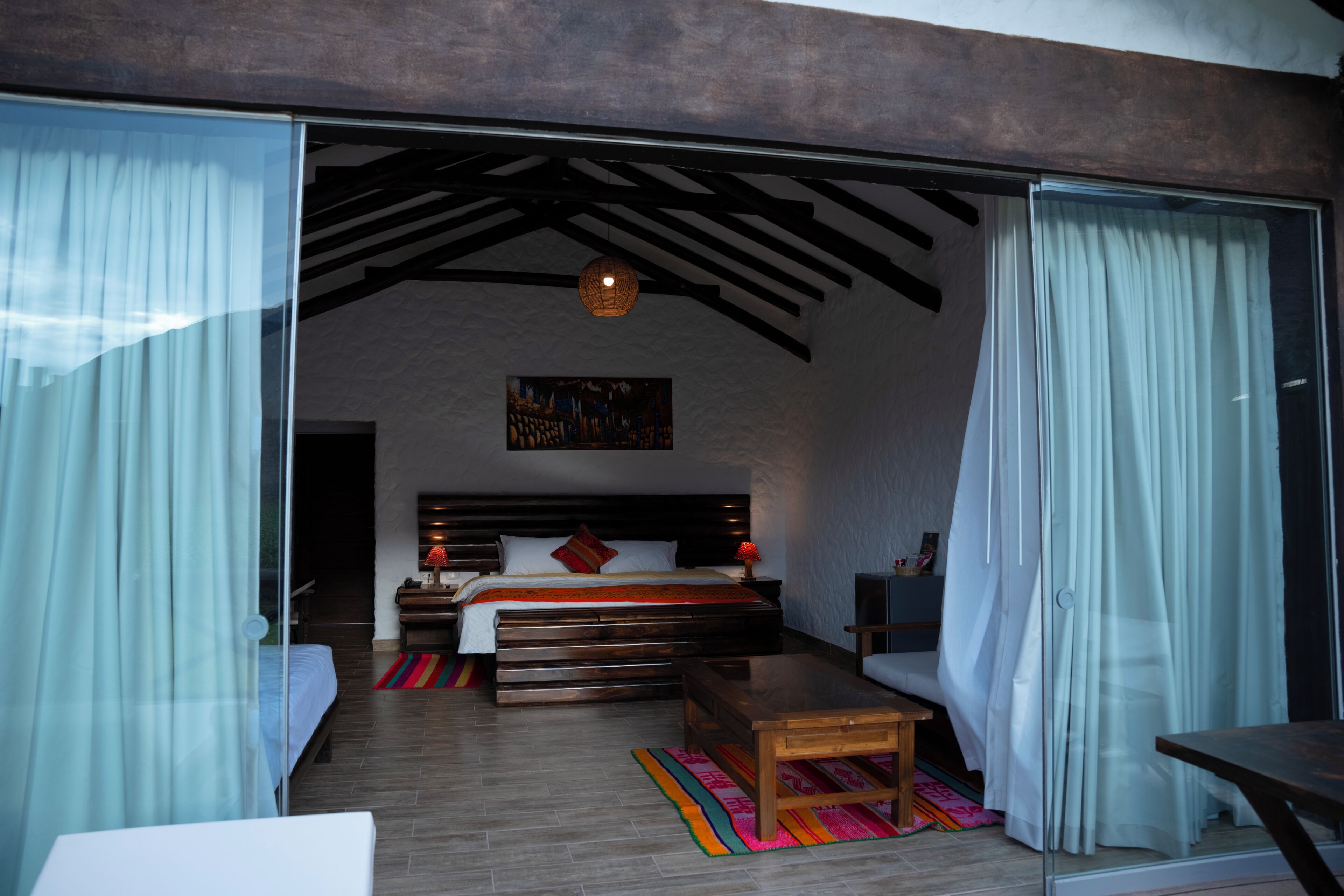 A bedroom with a bed, a wooden bench, a table, and a hanging light fixture.
