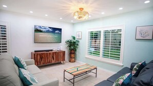 A modern living room with a television, a wooden cabinet, a bench, and a large window with blinds.
