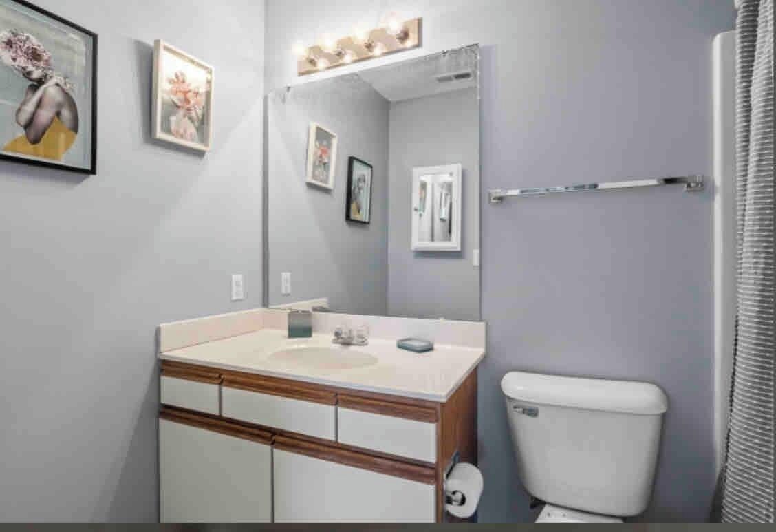 Une salle de bain avec un lavabo, un miroir, des toilettes et des tableaux encadrés accrochés au mur.