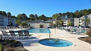 Un espace piscine avec des chaises longues, un jacuzzi et un bâtiment à plusieurs étages.