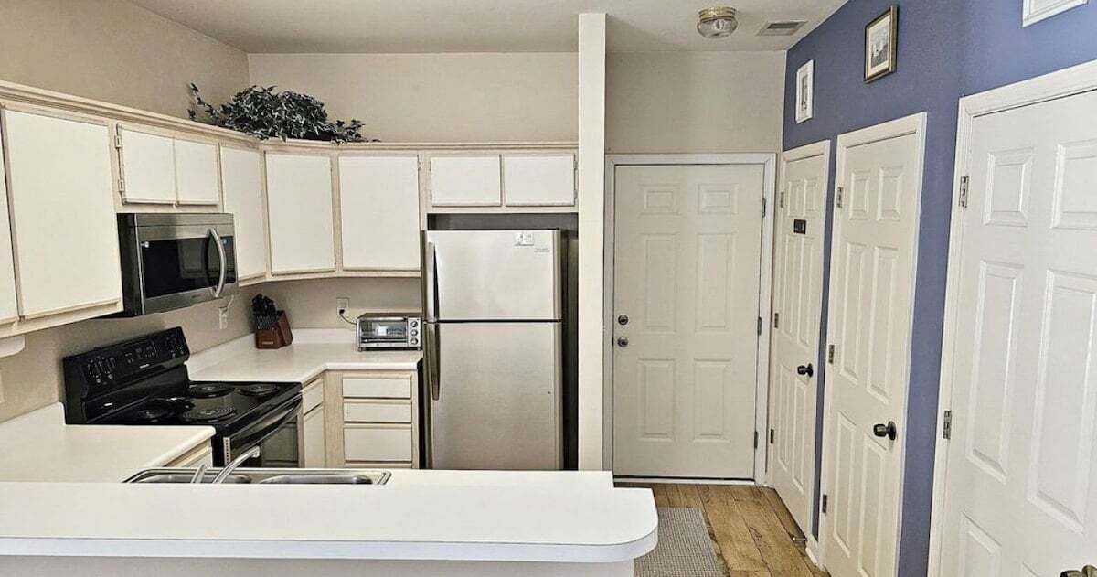 A compact kitchen with white cabinets, a microwave, a stove, a refrigerator, and a toaster.