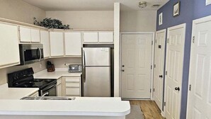 Une cuisine compacte avec des meubles blancs, un four à micro-ondes, une cuisinière, un réfrigérateur et un grille-pain.