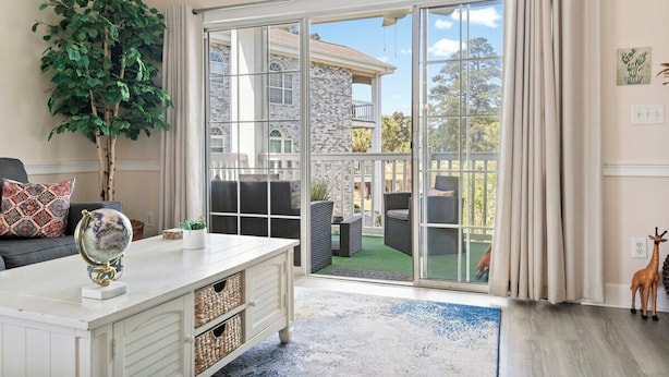 Un salon comprenant un canapé, une table basse, une plante en pot et une porte-fenêtre coulissante donnant sur une terrasse extérieure.