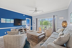 A living room with a television, a ceiling fan, a wooden coffee table, and a sofa. - Captains Quarters | Private Balcony + Resort Pool (Myrtle Beach)