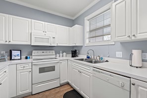 A modern kitchen with white cabinetry, a built-in oven, a microwave, a coffee maker, and a sink.