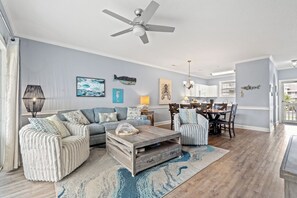A living room with a sofa, coffee table, and artwork on the wall. - Captains Quarters | Private Balcony + Resort Pool (Myrtle Beach)