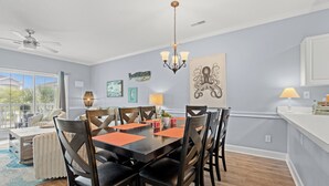 A dining area with a table set for six, surrounded by chairs, a chandelier, and wall art. - Captains Quarters In Myrtlewood Villas (Myrtle Beach)