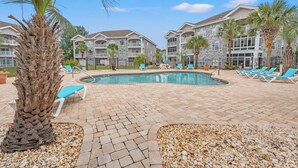 A pool area with lounge chairs, palm trees, and a building with a stone facade. - Captains Quarters In Myrtlewood Villas (Myrtle Beach)