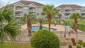 A hotel with a pool area, palm trees, and a fenced deck. - Captains Quarters In Myrtlewood Villas (Myrtle Beach)