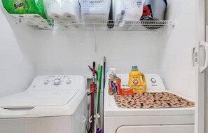 Un espace buanderie comprenant un lave-linge, un sèche-linge et une étagère où sont rangés les produits de nettoyage.