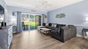 A living room with a sofa, a coffee table, a ceiling fan, and a sliding glass door leading to a patio.