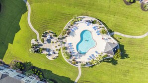 An aerial view of a resort with a swimming pool, sun loungers, and a well-maintained lawn.