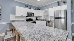 A kitchen with granite countertops, white cabinets, stainless steel appliances, and decorative wall art.