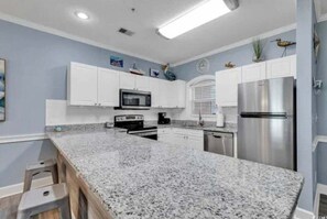 Une cuisine dotée de plans de travail en granit, de meubles blancs, d’appareils électroménagers en acier inoxydable et d’œuvres d’art décoratives sur les murs.